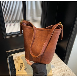Detail of vintage brown leather bucket bag with wide shoulder strap and gold metal hardware