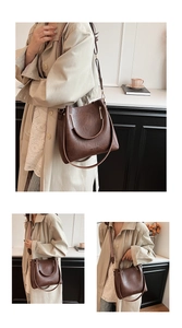 Detail of a brown bucket bag showing circular metal handles and a textured woven shoulder strap