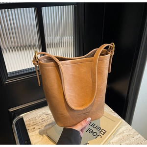 Detail of a brown leather bucket bag with adjustable strap on a marble surface