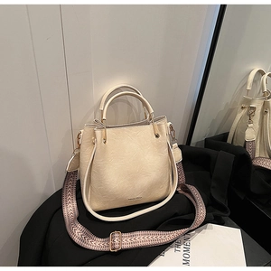 Detail of cream bucket bag with wide wavy strap and gold hardware on textured leather