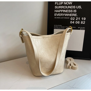 Detail of cream bucket bag with gold hardware and extra shoulder strap on marble surface