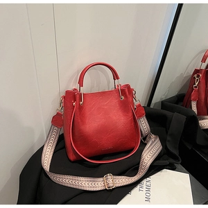 Detail of red bucket bag with unique metal handle and colorful woven shoulder strap