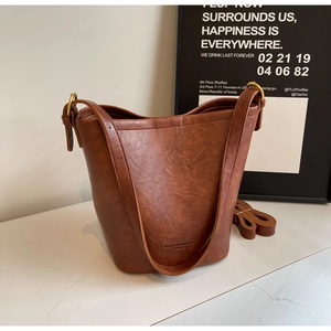 Detail of a brown PU leather bucket bag showing wave-shaped rim and gold-tone hardware buckle
