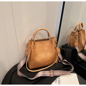 Detail of camel bucket bag featuring geometric wide strap and metallic logo accent