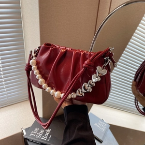 Burgundy ruched underarm bag with pearl chain and silver heart charm on a vanity table