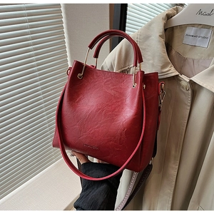 Detail of dark red bucket bag with textured leather, brand logo and metal ring handle
