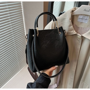 Detail of black leather bucket bag with gold hardware and herringbone fabric strap