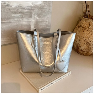 Detail of silver textured tote bag with heart pendant resting on art books
