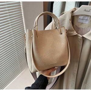 Detail of beige bucket bag with DINALISHA logo, woven strap, and gold metal hardware