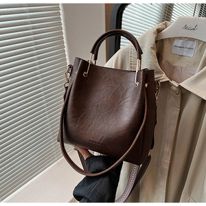 Detail of a brown bucket bag showing the texture, DINALISHA logo, and metal handle