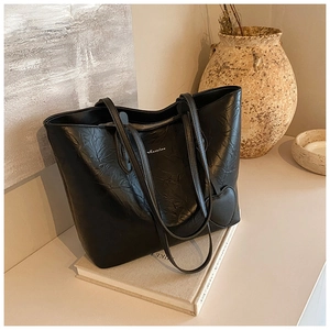 Detail of black pleated faux leather tote bag with heart charm on books