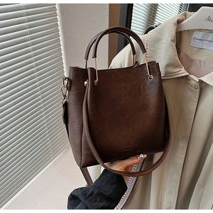 Detail of dark brown bucket bag featuring gold hardware and removable wide shoulder strap