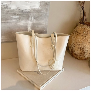Detail of cream tote bag with wrinkled leather texture and heart-shaped charm on books