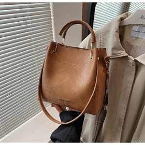 Detail of caramel brown bucket bag with gold metal handle and logo embossing