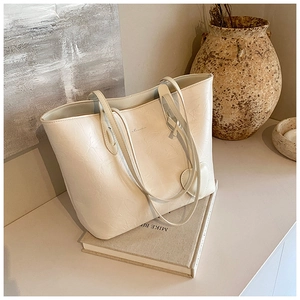 Detail of cream tote bag with crinkled leather texture and heart-shaped charm accessory