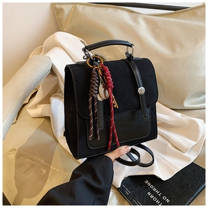 Detail of black suede backpack featuring woven cord charms and tennis racket pendant
