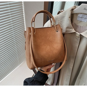 Detail of caramel brown bucket bag with metal handle attachments and Dinalisha logo