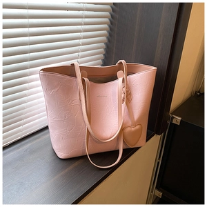 Detail of pink textured tote bag with heart charm and brand logo under soft window light