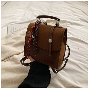 Detail view of brown matte backpack featuring silver metal buckle and woven cord pendant