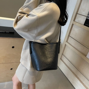 Minimalist black leather bucket bag with pleated texture shown as a stylish crossbody bag
