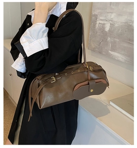 Detail view of dark brown leather cylinder shoulder bag with vintage buckles on a model