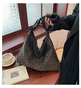 Detail of leopard print tote bag with black pleated handle on a wooden cafe table
