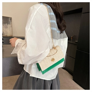 Detailed view of woven straw crossbody bag with green leather base and gold metal handle
