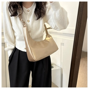 Chic golden crescent shoulder bag with ruched strap detail on casual knitwear