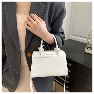Close-up of a white trapezoid handbag with knot handle and Fashion Bag gold lettering