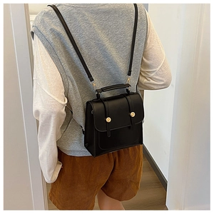Detailed view of a black mini backpack with golden metal fastener worn by a model