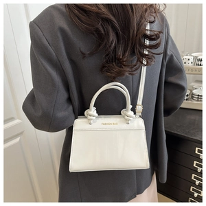 Detail of a white minimalist square bag with gold lettering and knotted handle