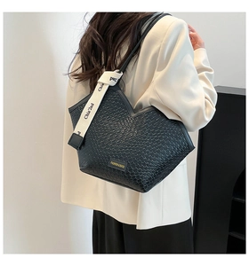 Detalle de bolso negro trenzado con correa de lona crema y diseño de corte en V superior