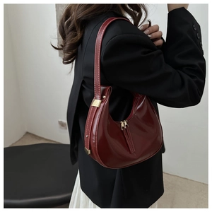 Detail of burgundy patent leather crescent bag with gold hardware on black blazer outfit