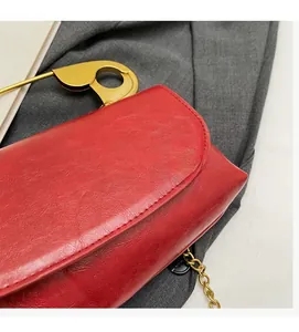 Detalle del bolso de cuero rojo con gran imperdible dorado y correa de cadena fina