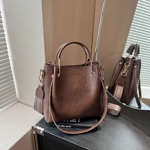 Dark brown leather bucket bag with top handle and stylish striped woven shoulder strap