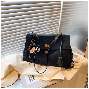 Detail of black suede tote bag with gold swivel locks and a baseball charm pendant
