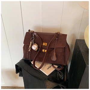 Close-up of brown suede tote bag with double gold twist locks and baseball charm