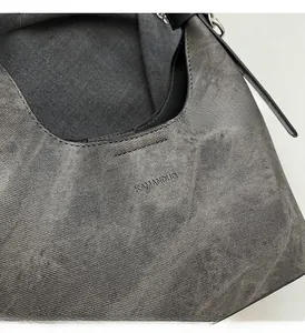 Detail der grauen Twill-Schultertasche mit Logo-Prägung und silberner Kettenriemen