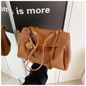 Detail of caramel brown suede tote bag featuring dual metal locks and woven pendant