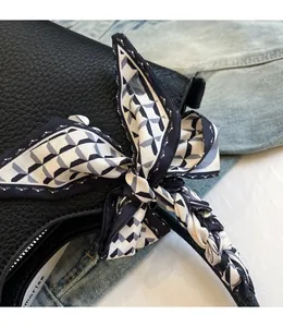 Détail d'un sac à main en cuir grainé noir avec une écharpe en soie nouée à l'anse