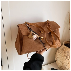 Detail of brown suede tote bag with gold metal clasp and sporty baseball charm