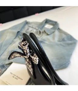 Gros plan des poignées de sac en cuir grainé noir avec un détail de foulard en soie