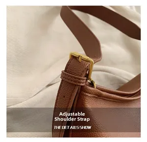 Close-up of adjustable shoulder strap with gold buckle on brown lychee leather bag