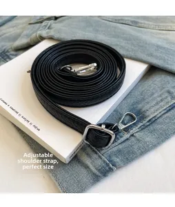 Détail de la bandoulière réglable en cuir noir avec boucles argentées sur fond denim