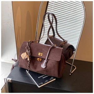 Detailed close-up of dark brown suede tote with gold square locks and baseball charm