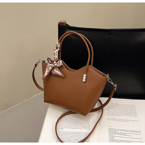 Détail du sac seau en cuir grainé marron avec poignée ornée d'un foulard en soie chic