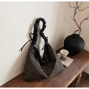 Detail of leopard print tote bag with black scrunchie strap on a wooden bench