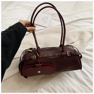 Detailed close-up of wine red cylindrical shoulder bag with gold buckles and accessory pouch