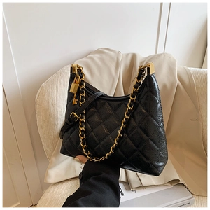 Close-up of black quilted leather bag with gold chain and key charm on white suit