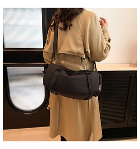 Détail d'un sac bandoulière en nylon noir avec sangle réglable porté sur un trench